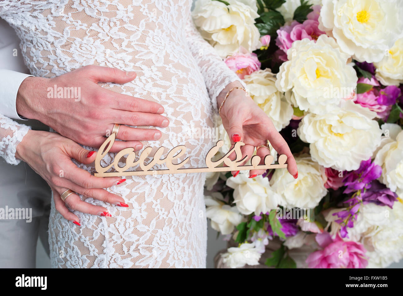 man in is tenderly embracing his pregnant wife near wall of flowers ...