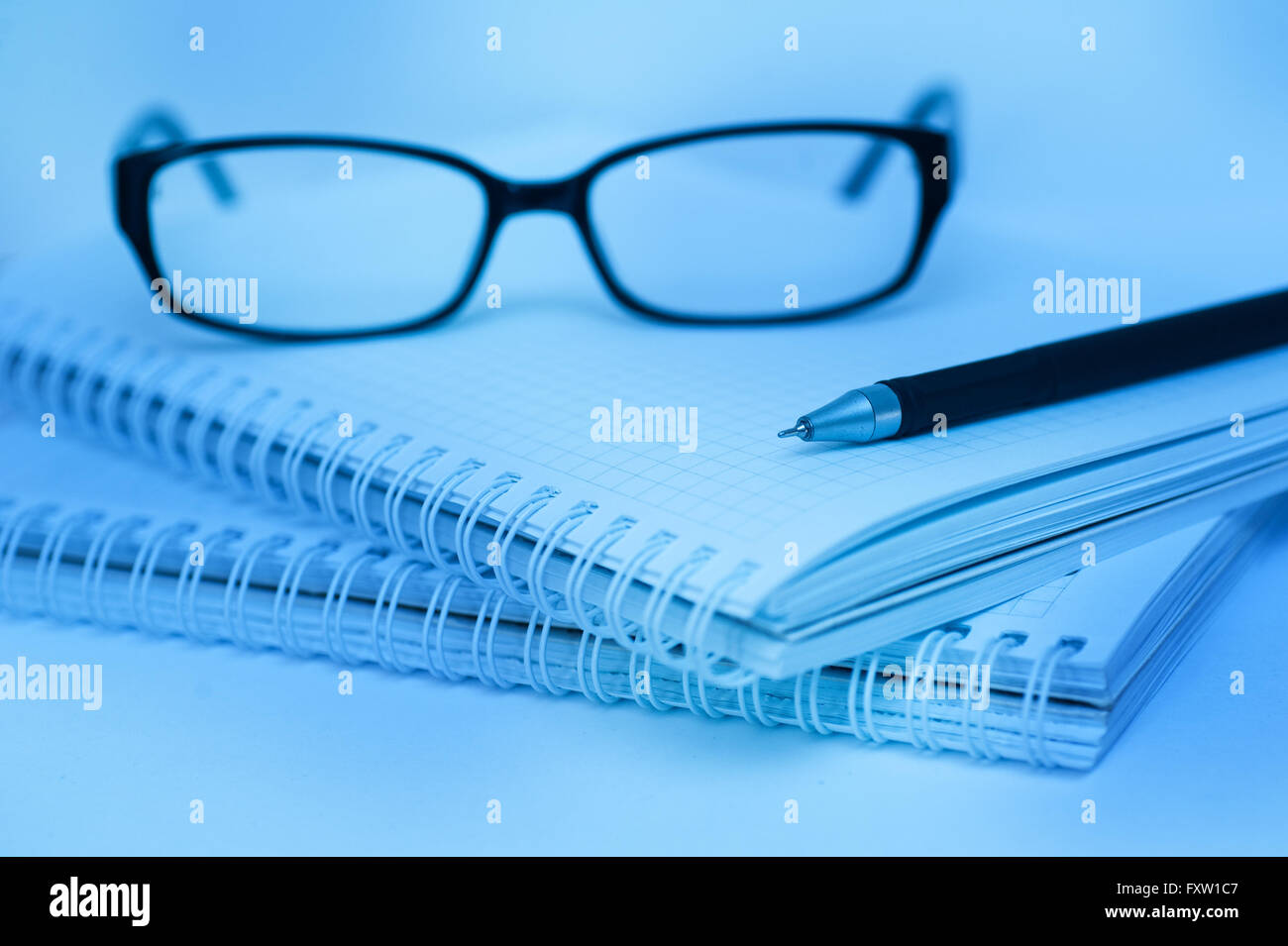 black pen and glasses lying on notebook close up blue color Stock Photo