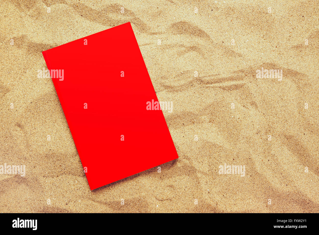 Book with red covers on summer vacation beach holiday, top view of a book in warm beach snow as copy space Stock Photo
