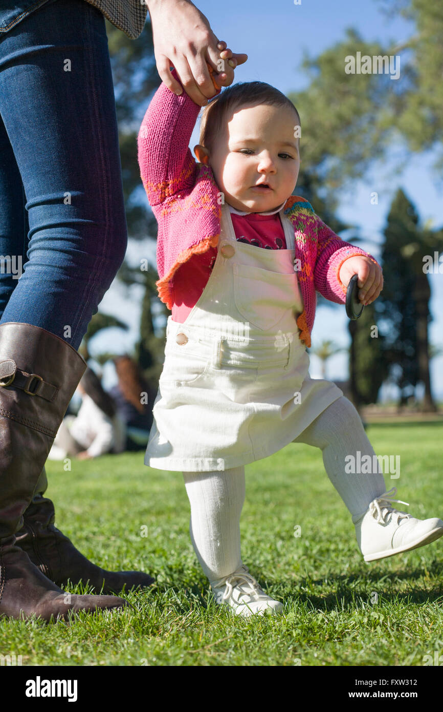 Cute baby girl learning to walk over the grass park on springtime Stock Photo