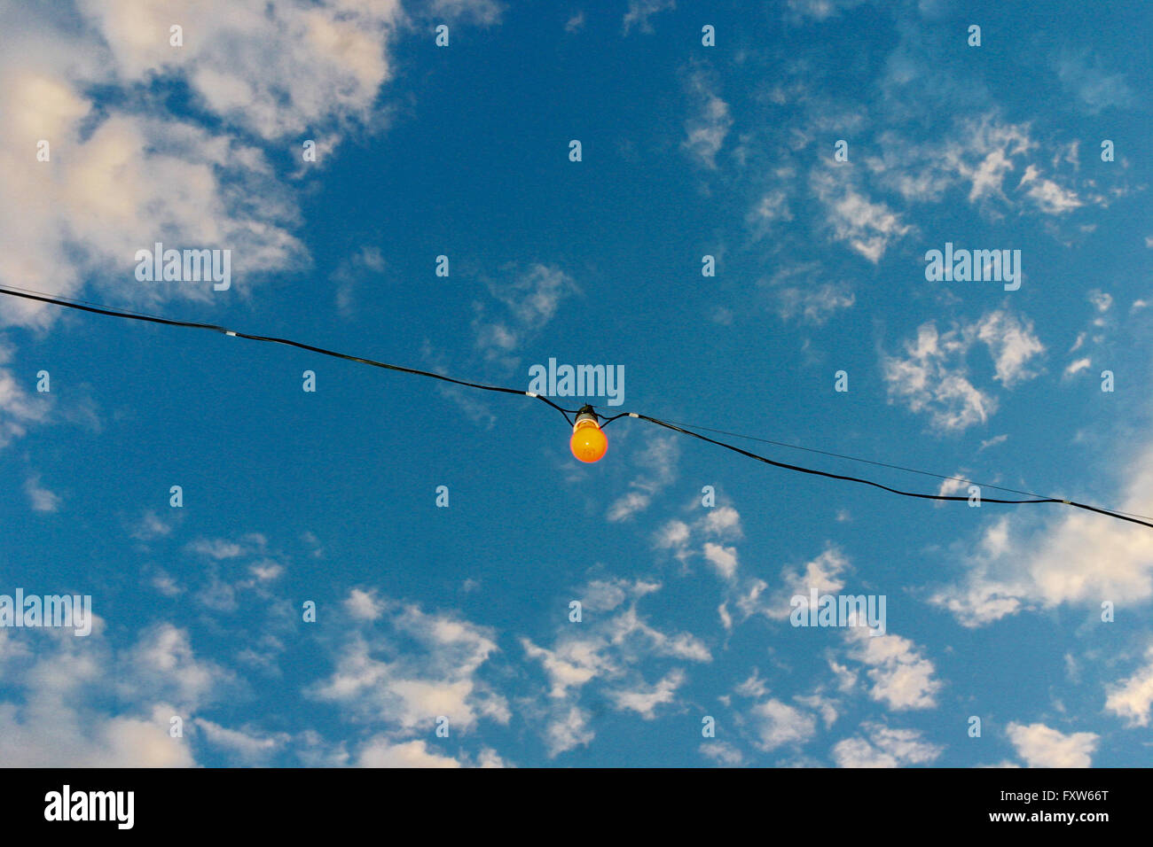 The single orange bulb sky on wire line, clouds in the blue sky background looking up to sky, bulb concept Stock Photo
