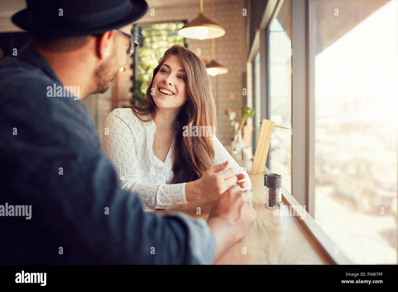 Smiling young woman sitting in a cafe and talking to her boyfriend. Young couple spending time at coffee shop. Stock Photo