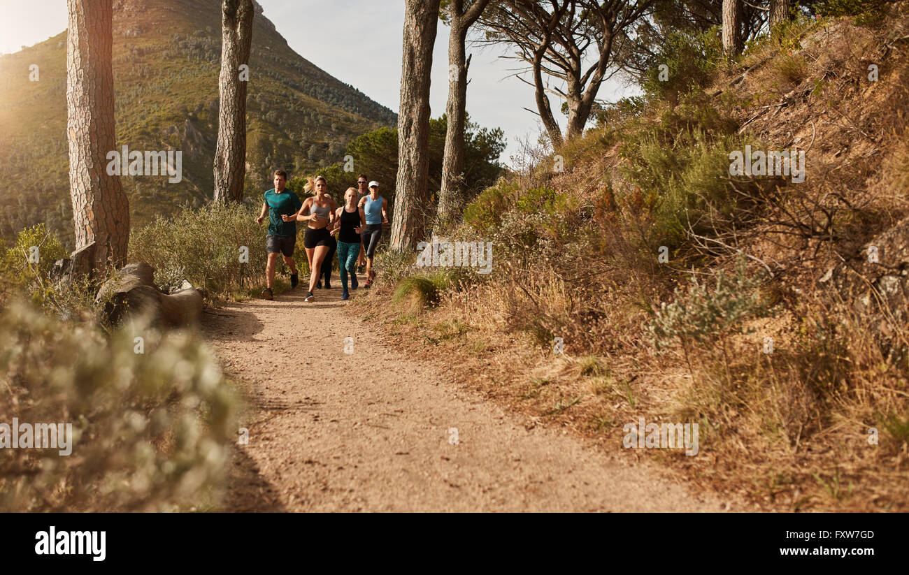 Group of athletes running together through trails on the hillside. Young people trail running on a mountain path outdoors. Stock Photo