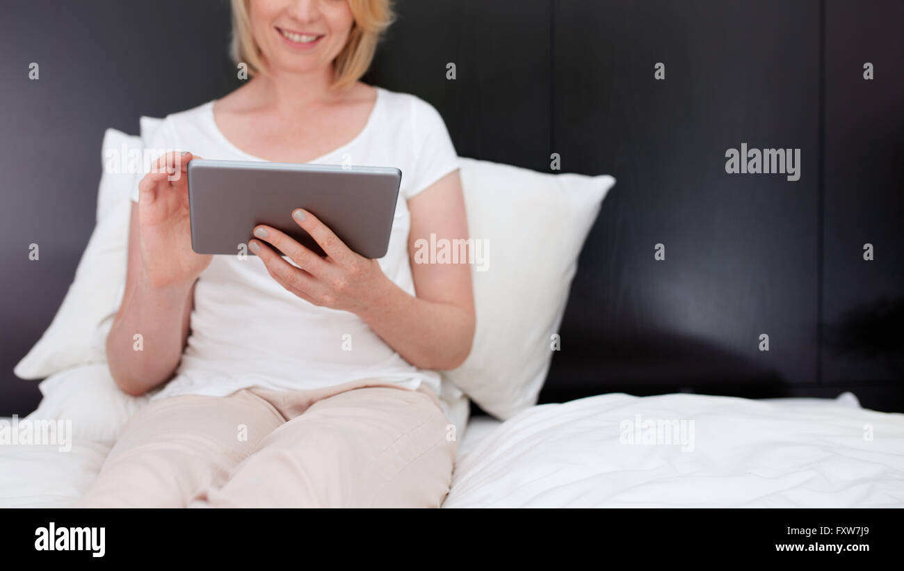 Cropped shot of woman using digital tablet, she is sitting on bed. Stock Photo