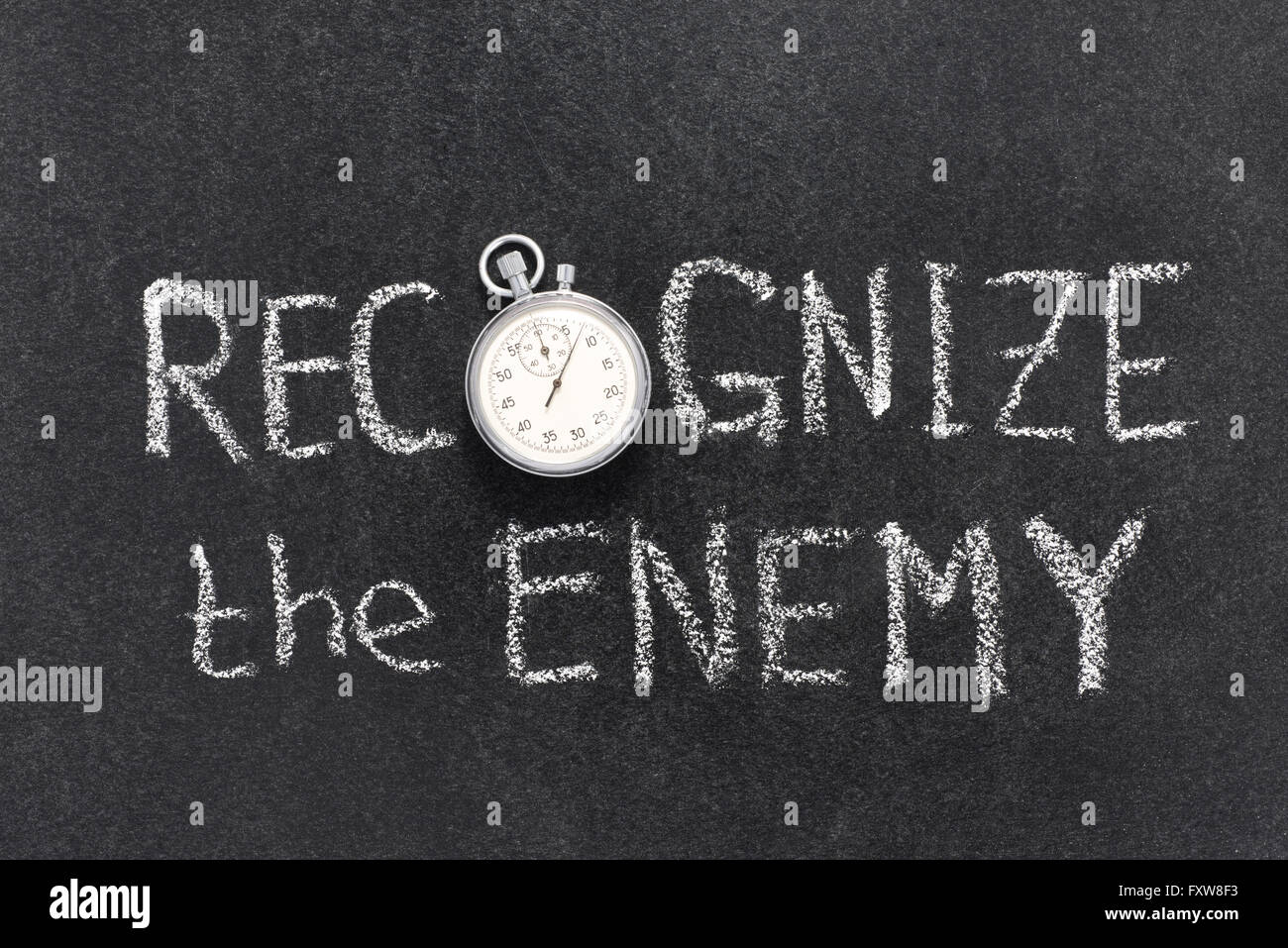 recognize the enemy phrase handwritten on chalkboard with vintage precise stopwatch used instead of O Stock Photo