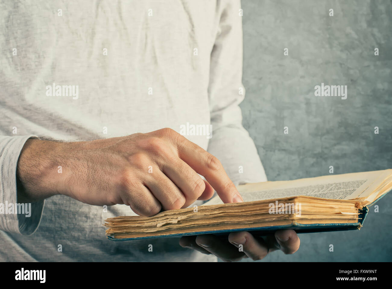 Man reading old book with torn pages, close up of adult male hands holding vintage book. Stock Photo