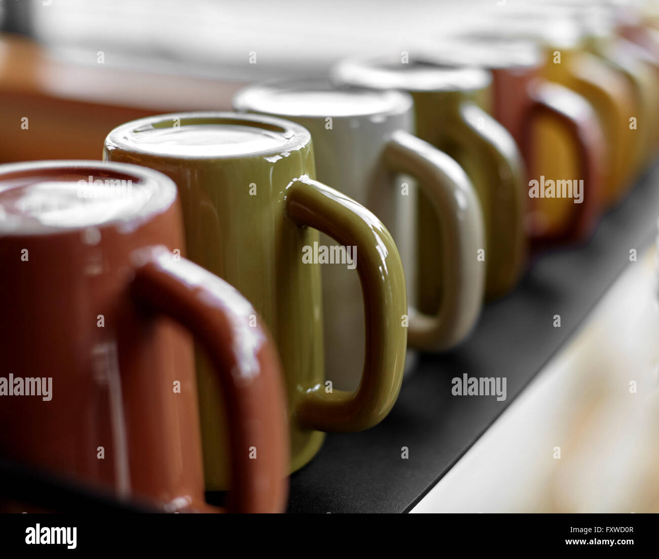 Black shelf lined with multi colored ceramic coffee mugs Stock Photo