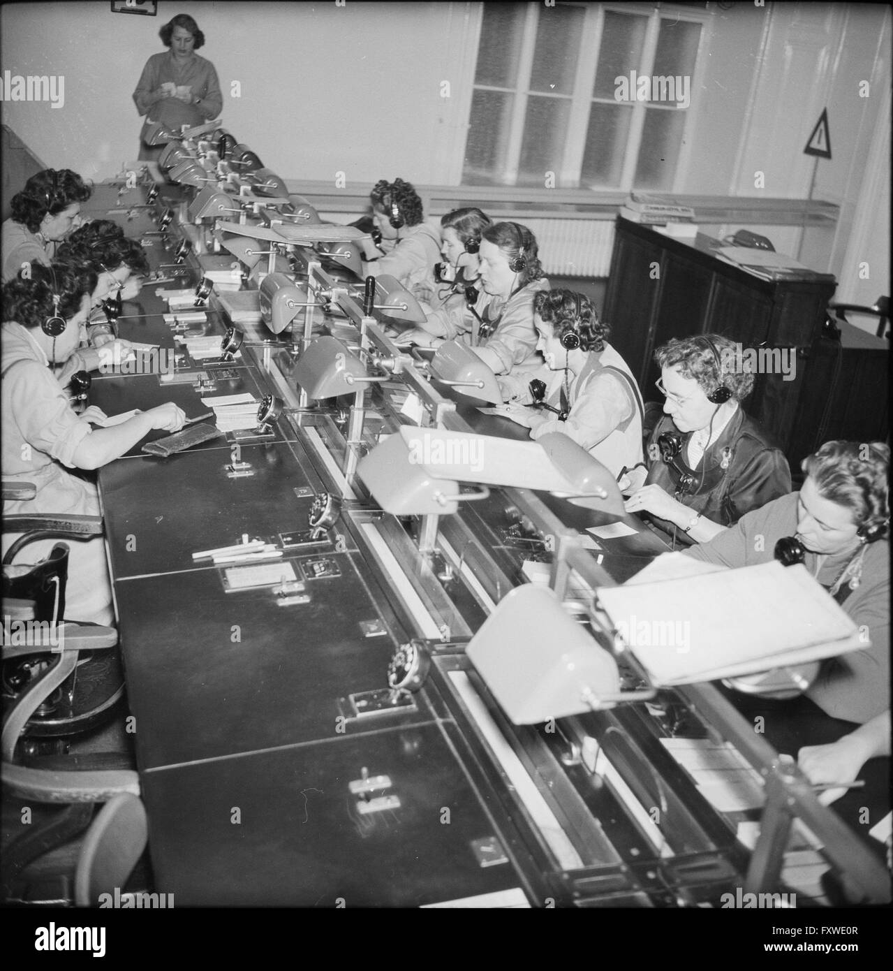 Telefonistinnen sitzen an einem langen Tisch ... Stock Photo