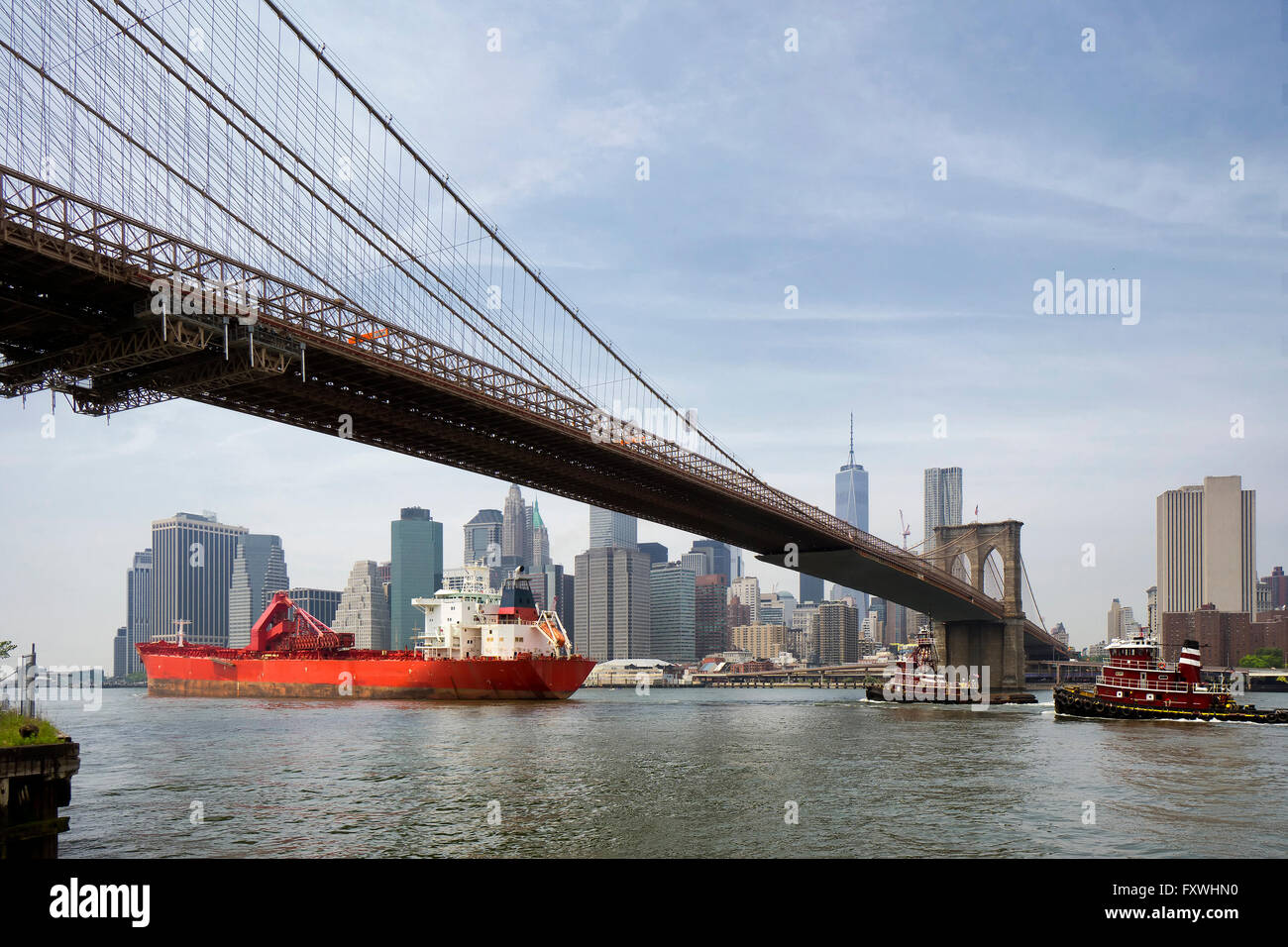 cargo ship and tug boat under brooklyn bridge, New York City Stock Photo