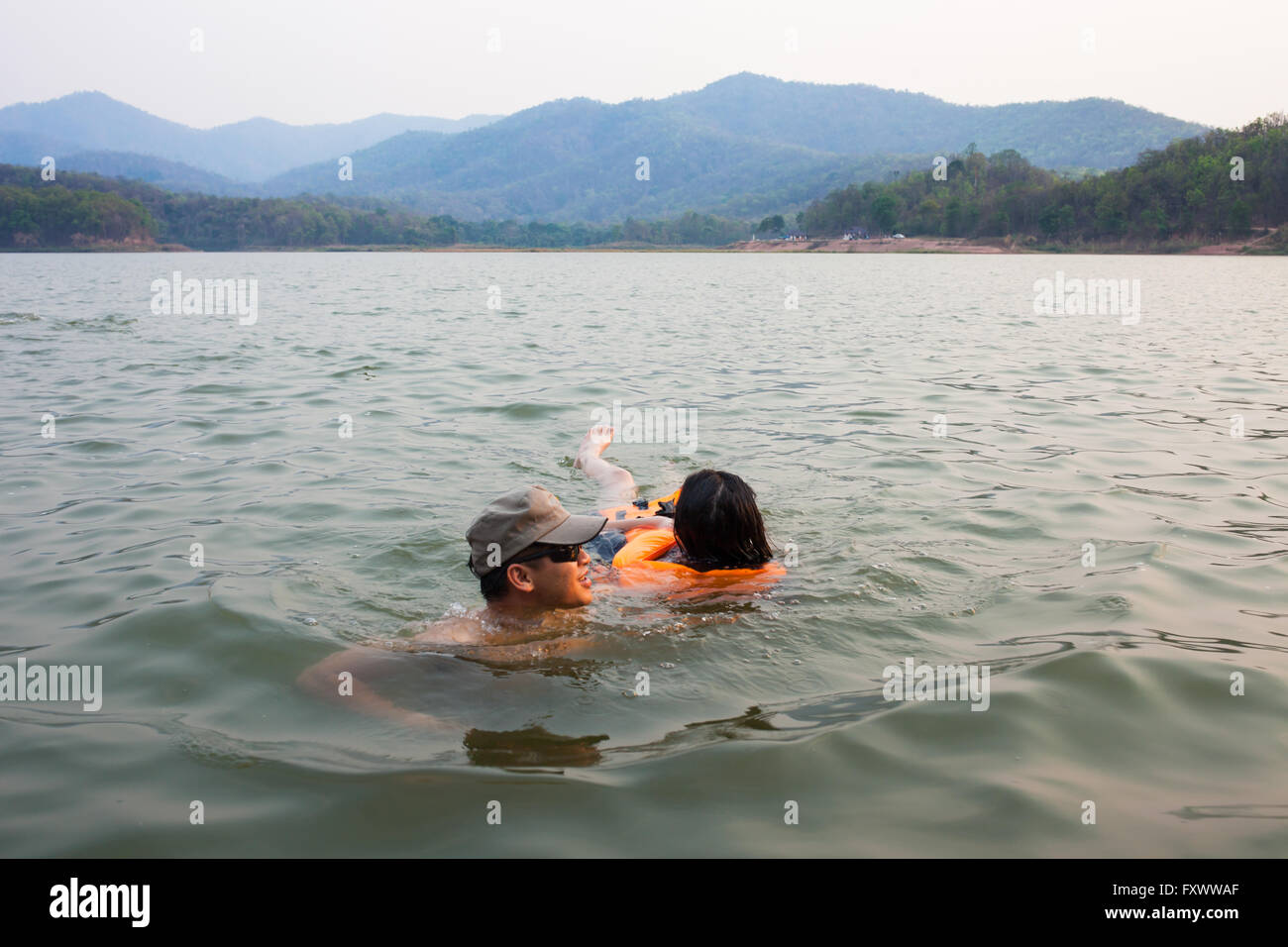 Phayao, Thailand - April 15, 2016. Man at river help women drowning due to water accidents by wearing a life jacket and escorted out of the water . Stock Photo