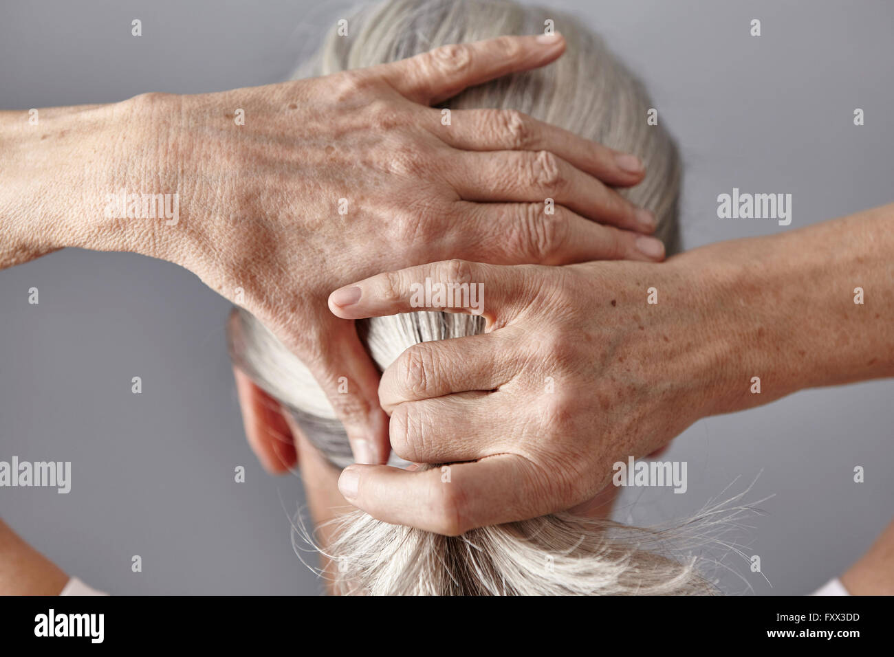 Rear view of woman pulling back gray hair into ponytail Stock Photo