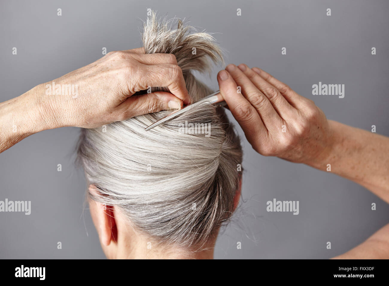 Rear view of woman styling gray hair into bun Stock Photo