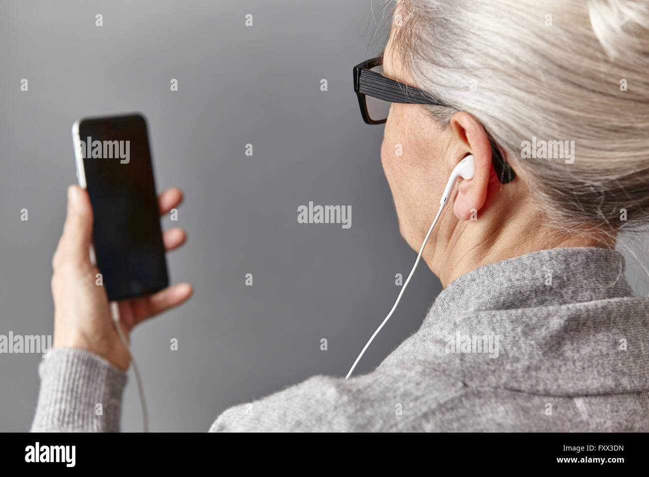 Over shoulder view of gray haired woman wearing ear buds holding smartphone Stock Photo