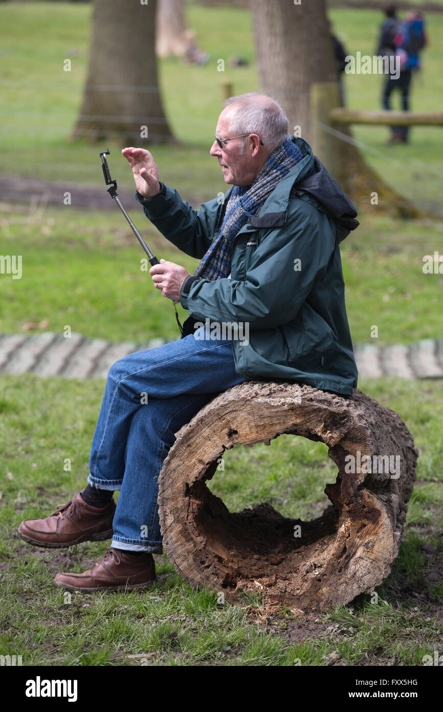 Pensioner using his smartphone on a selfie-stick outdoors at Hatchlands Park, Surrey, England, UK Stock Photo