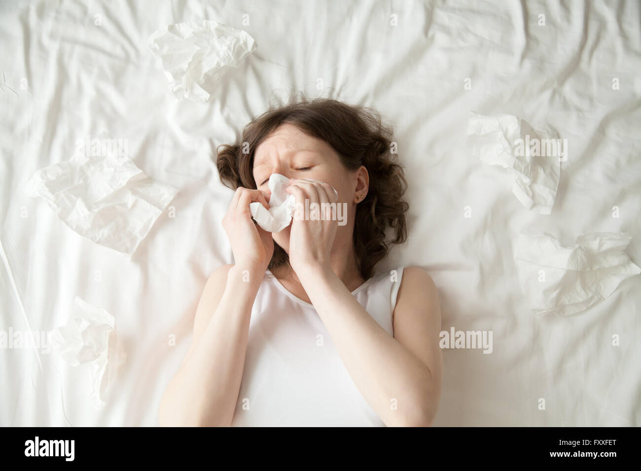 Young depressed or sick with flu model lying on the bed with closed eyes and blowing her nose into tissue. Stock Photo