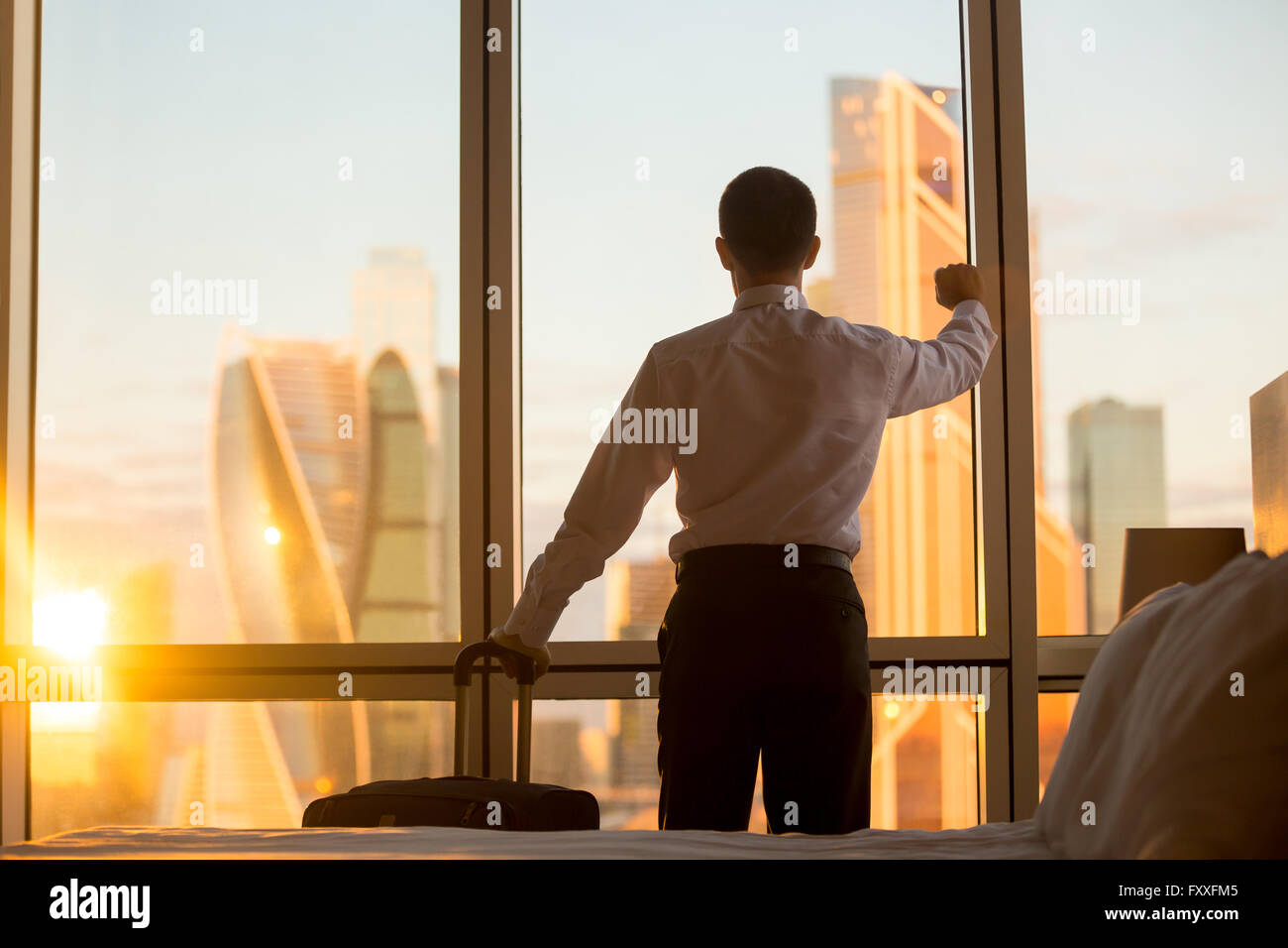 Morning in luxurious hotel. Rear view of handsome young businessman standing in confident pose at window in cozy room Stock Photo