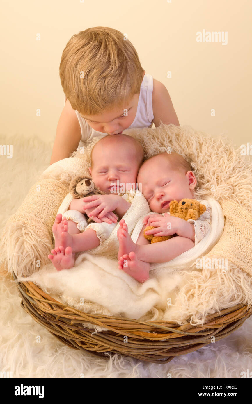 Toddler boy posing with his newborn identical twin sisters Stock Photo