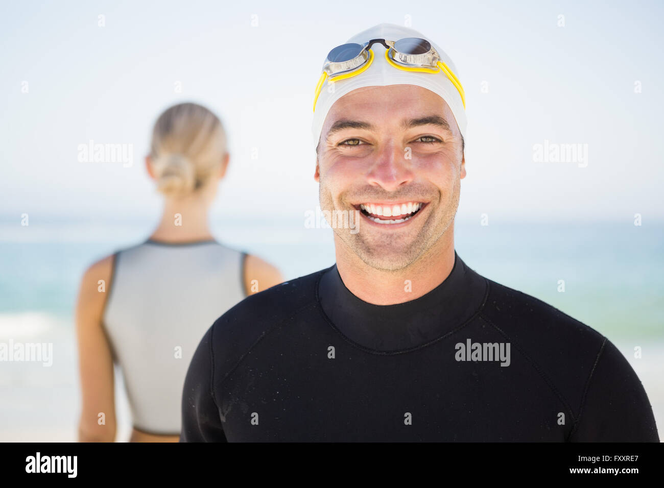 Handsome man wearing swimming cap and goggles with girlfriend in background Stock Photo