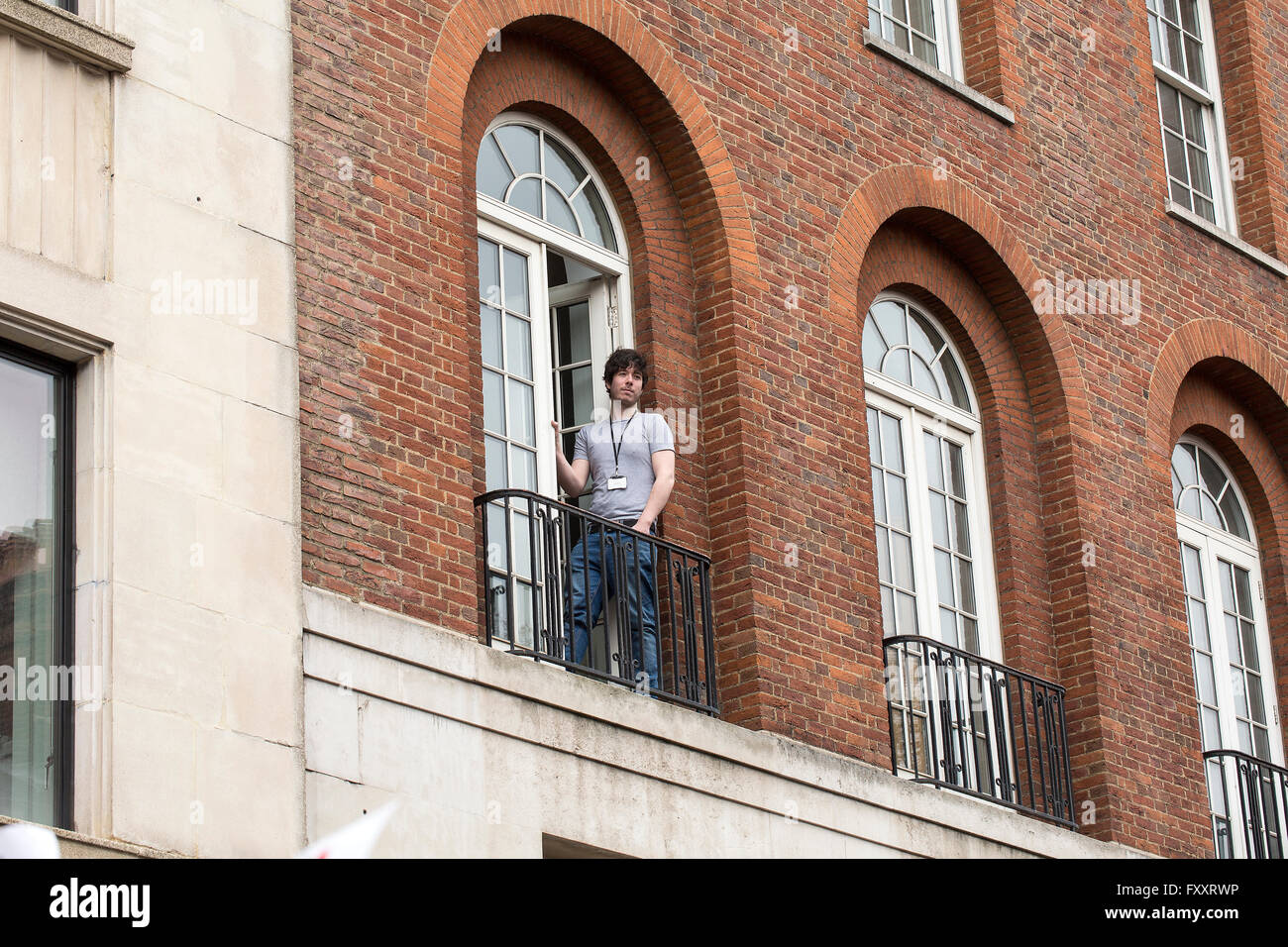 Anti-Austerity March. A young man watches from his apartment as the anti-austerity march passes by. Stock Photo