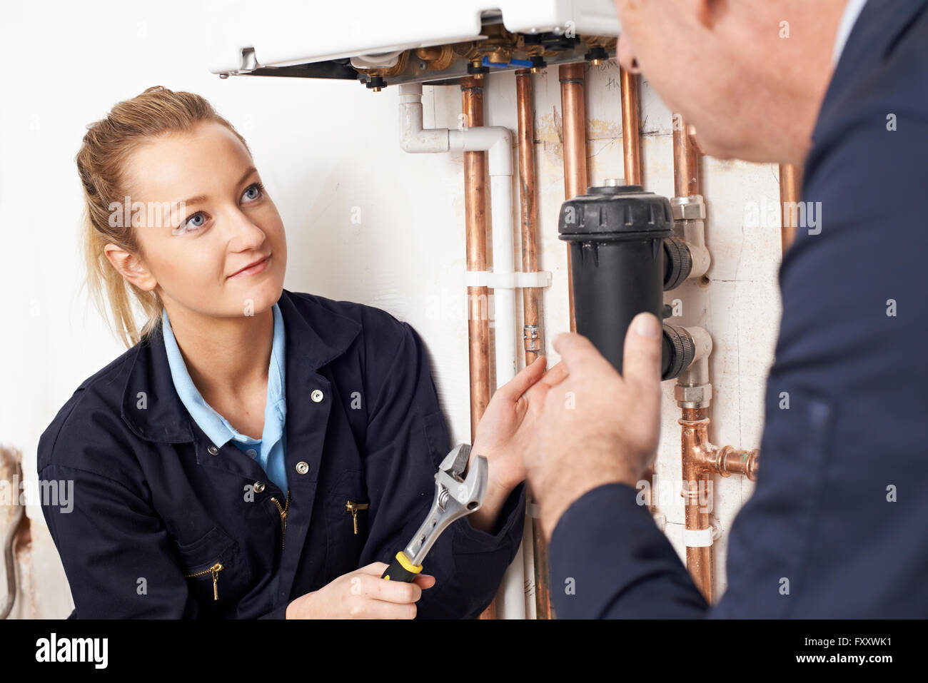 Female Trainee Plumber Working On Central Heating Boiler Stock Photo