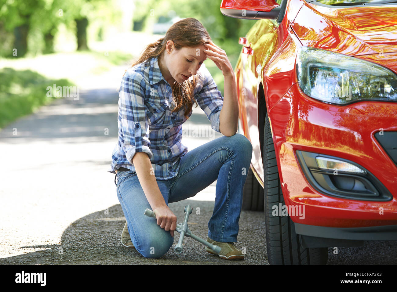 Frustrated Female Driver With Tyre Iron Trying To Change Wheel Stock Photo