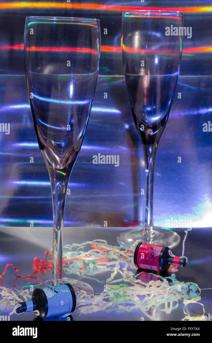 A Studio Photograph of Two Champagne Flutes and Party Poppers Set Against a Silver Holographic Backdrop Stock Photo