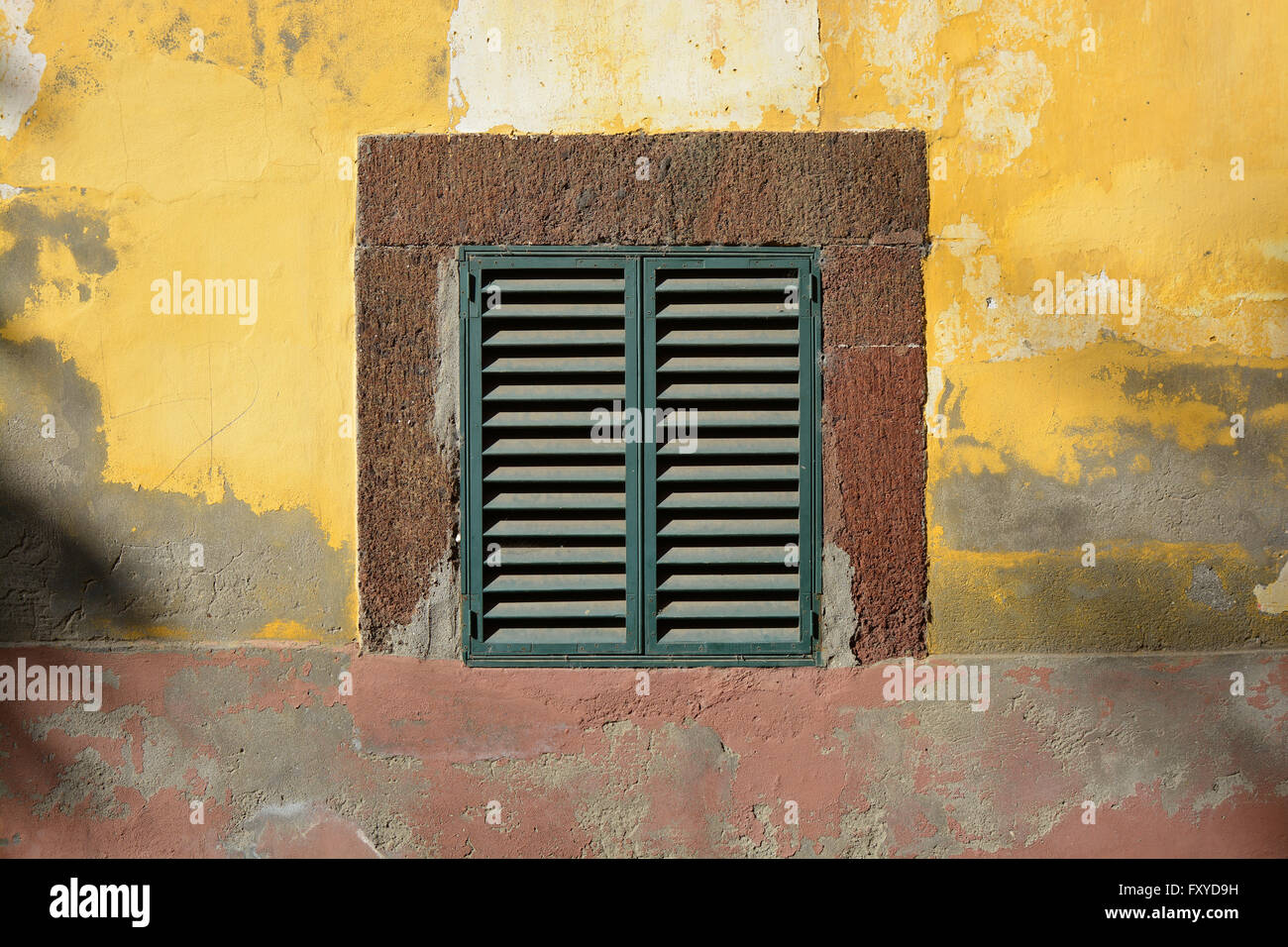 Closed shutters on window in weathered painted wall in old town of