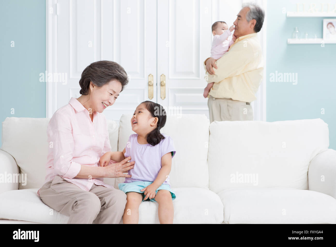 Grandmother having fun with her granddaughter and grandfather holding a baby behind them Stock Photo