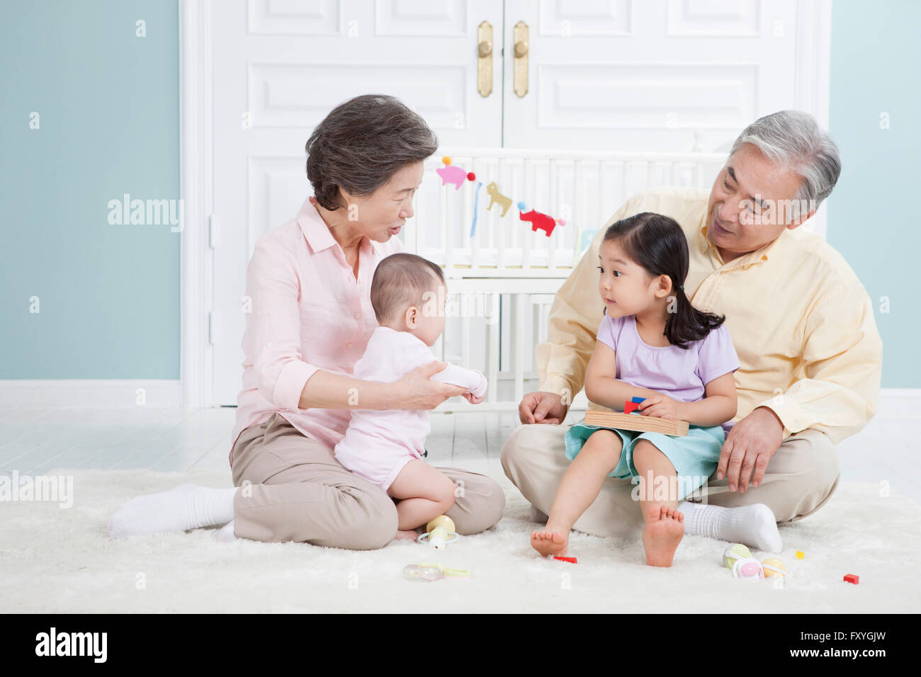 Grandparents and grandchildren having fun with toys together all seated on the floor in a room Stock Photo