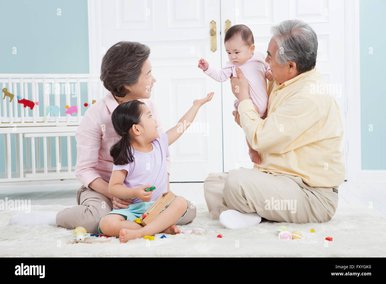Grandfather holding a baby and grandmother and granddaughter looking at the baby all seated on the floor Stock Photo