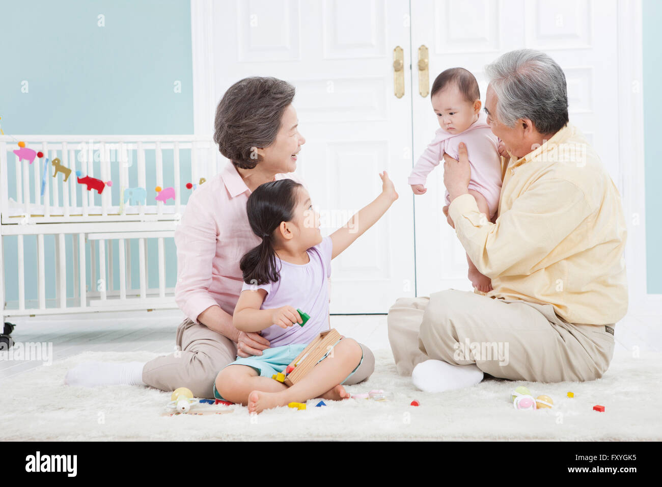 Grandfather holding a baby and grandmother and granddaughter looking at the baby all seated on the floor Stock Photo