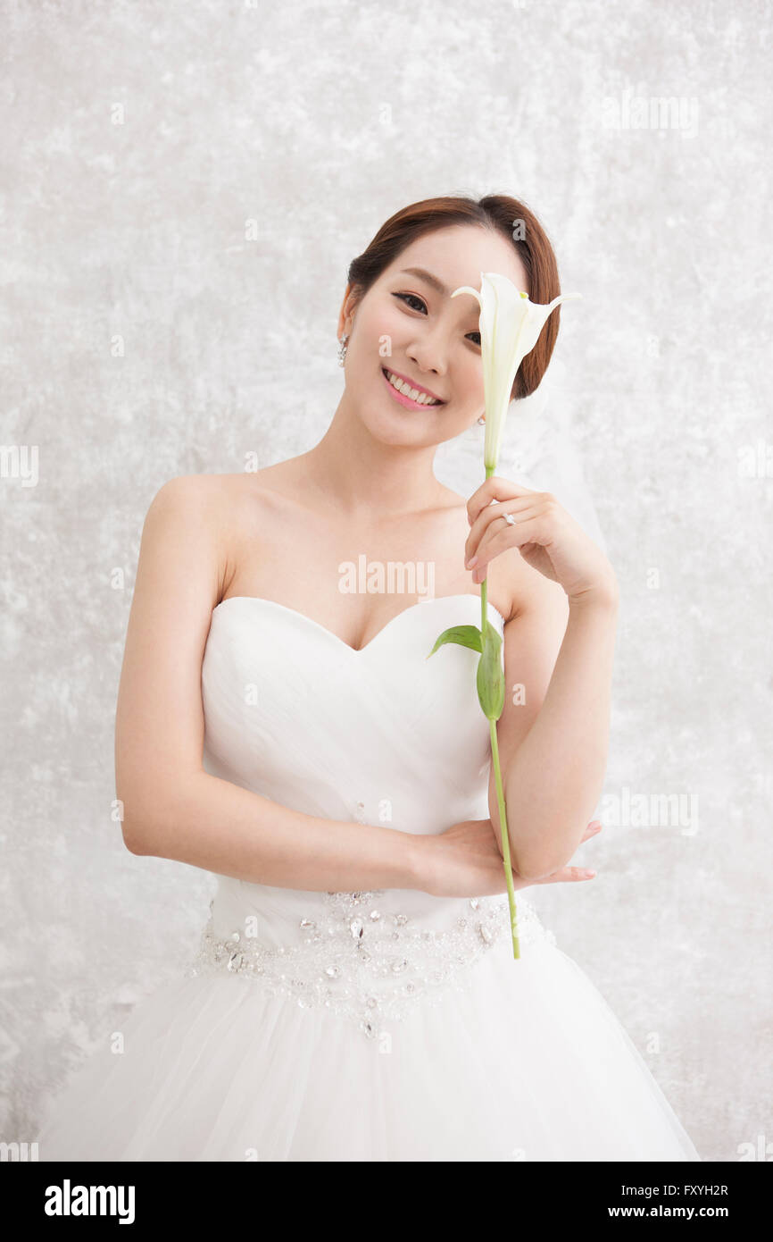 Bride holding a flower close to her face and staring forward with a smile Stock Photo