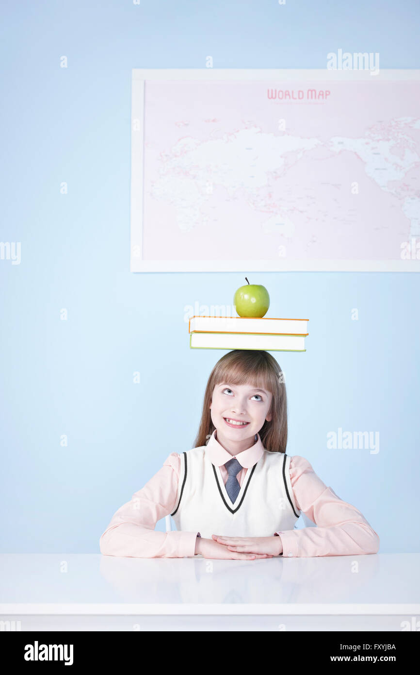Girl seated at desk with books and a green apple on her head Stock ...