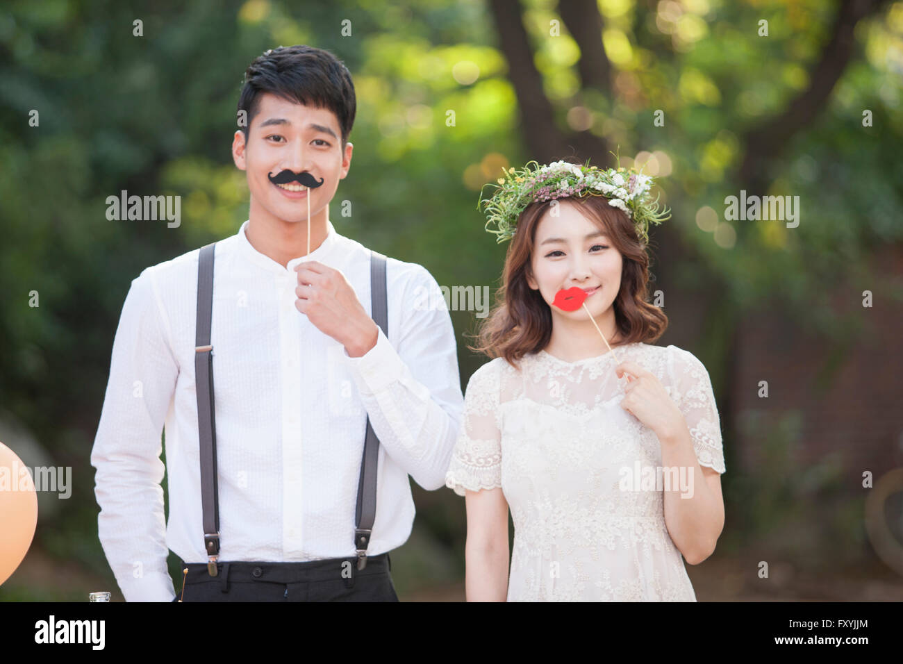 Bride and bridegroom together outside holding a fake mustache and fake lips Stock Photo
