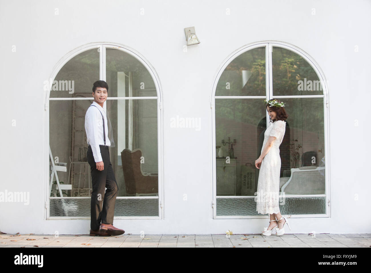 Bride and bridegroom standing by the building with big windows outside Stock Photo