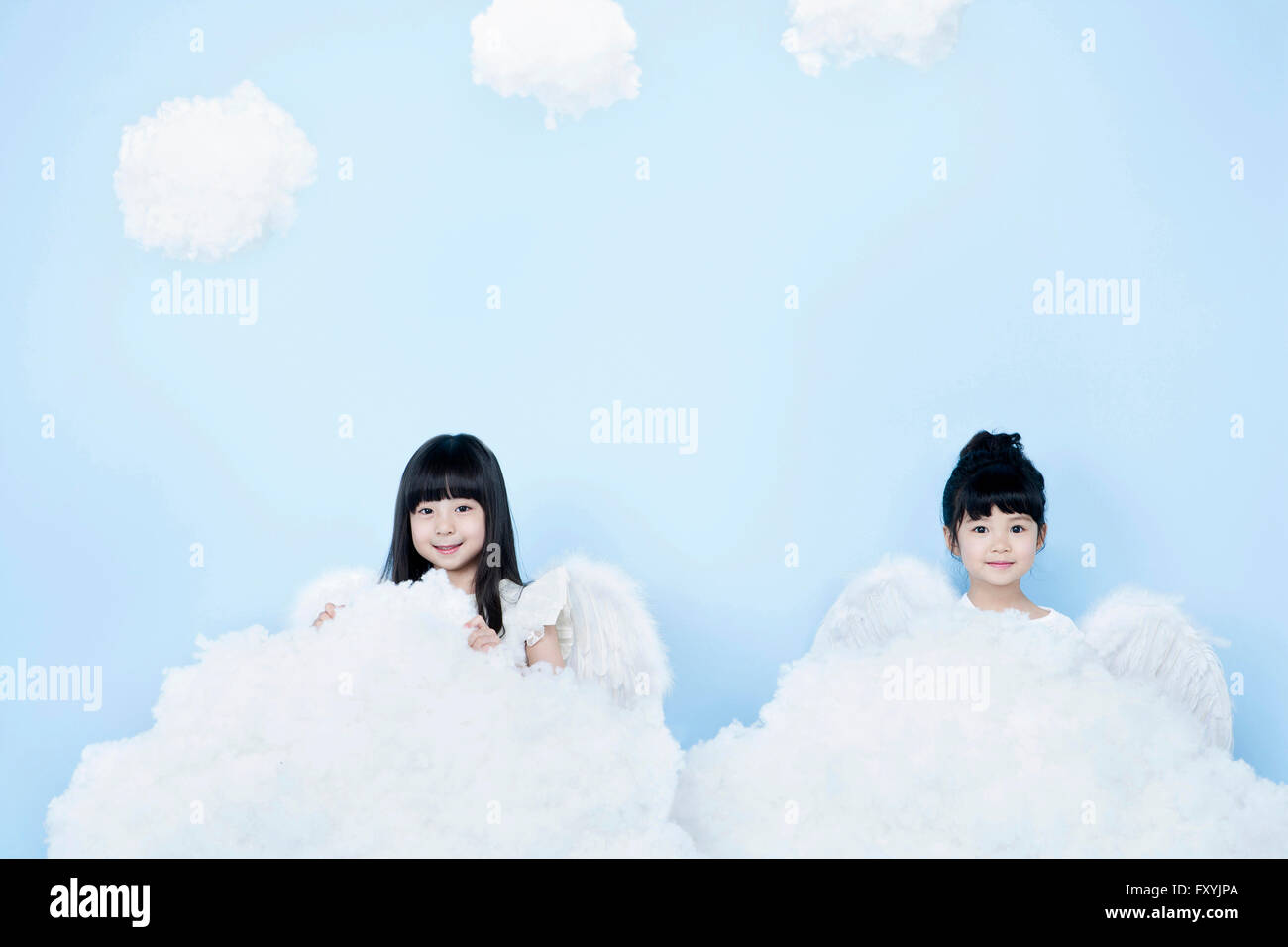Two girls in angel costume behind clouds in the background representing heaven Stock Photo