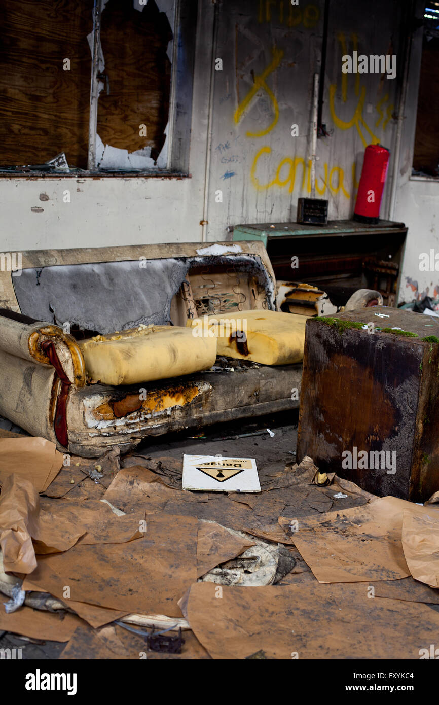 Burnt out sofa in a derelict building with lots of rubbish and a danger