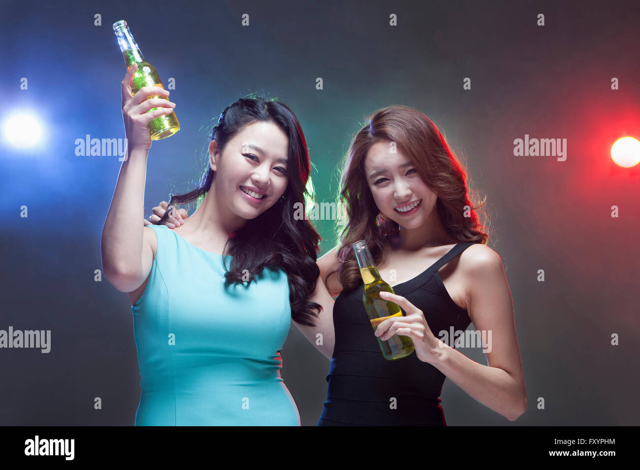 Portrait of two young smiling women holding beer bottles at nightclub Stock Photo