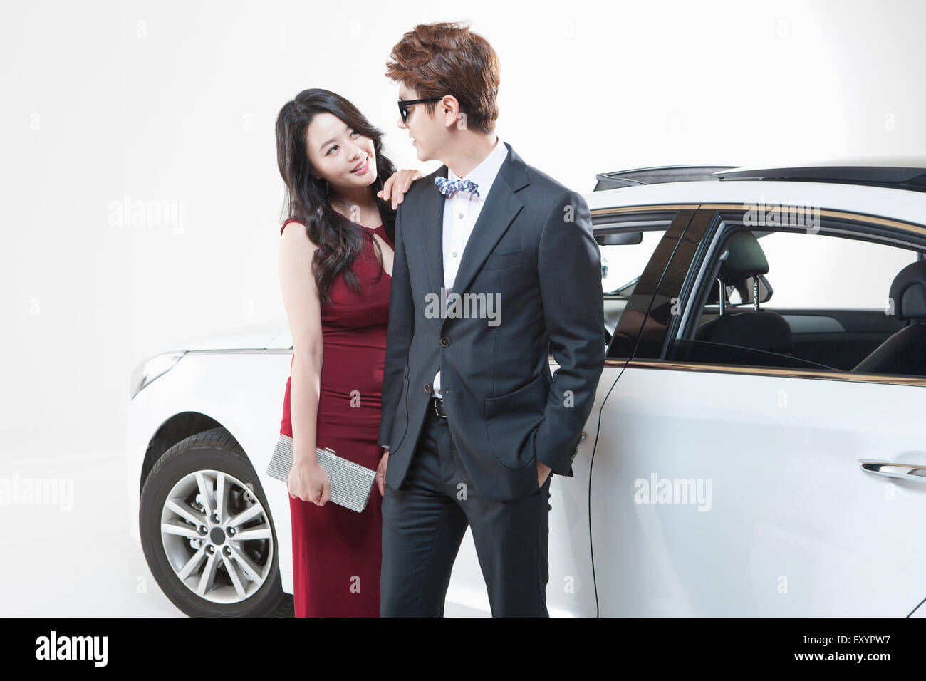 Young woman in dress and young man in suit smiling at each other in front of a fancy car Stock Photo