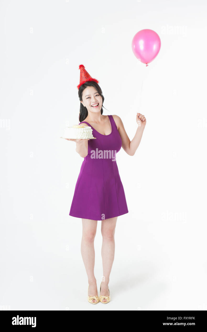 Young smiling woman with party hat holding a cake and a balloon Stock Photo
