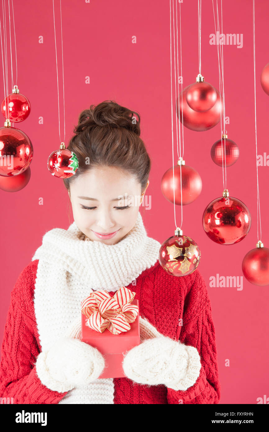 Portrait of young smiling woman wearing muffler and mittens looking down at present box inher hands with Christmas balls Stock Photo