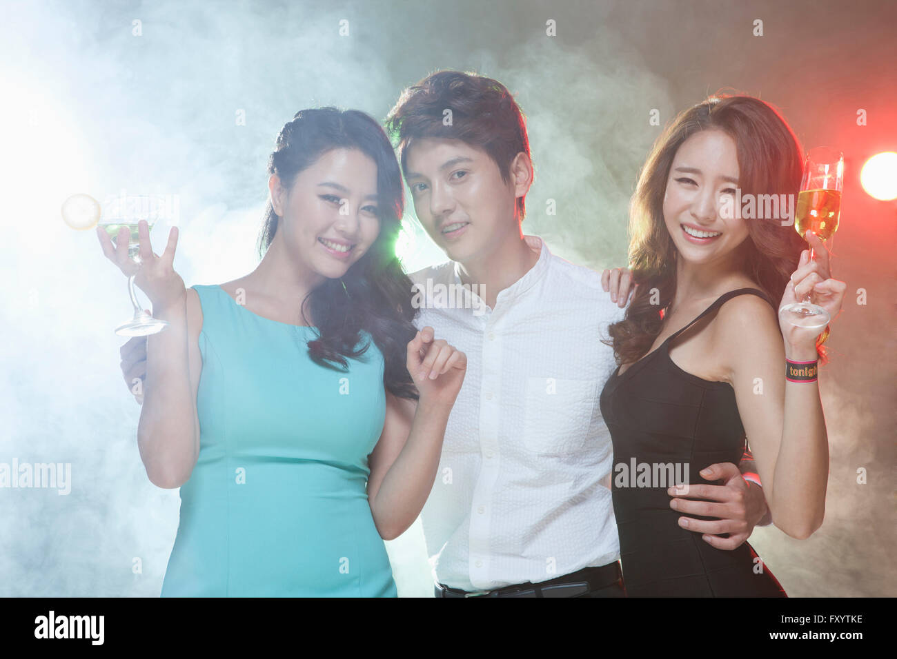 Portrait of three young smiling people posing with drinks at nightclub staring at front Stock Photo