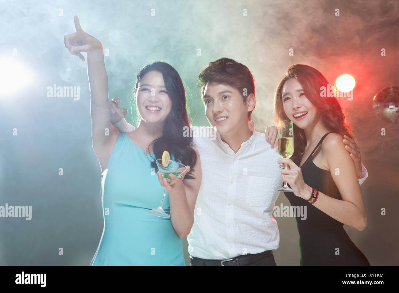 Portrait of three young smiling people posing with drinks looking up at nightclub Stock Photo