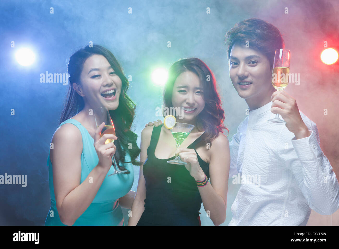 Portrait of three young smiling people posing with drinks staring at front at nightclub Stock Photo