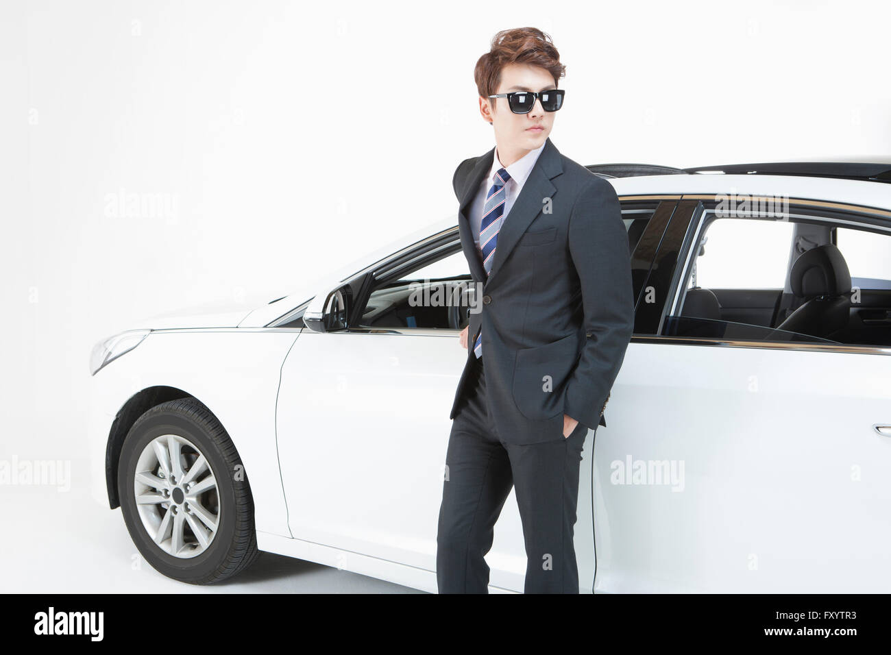 Side view of young man wearing sunglasses and suit standing with his hands in pockets in front of car Stock Photo
