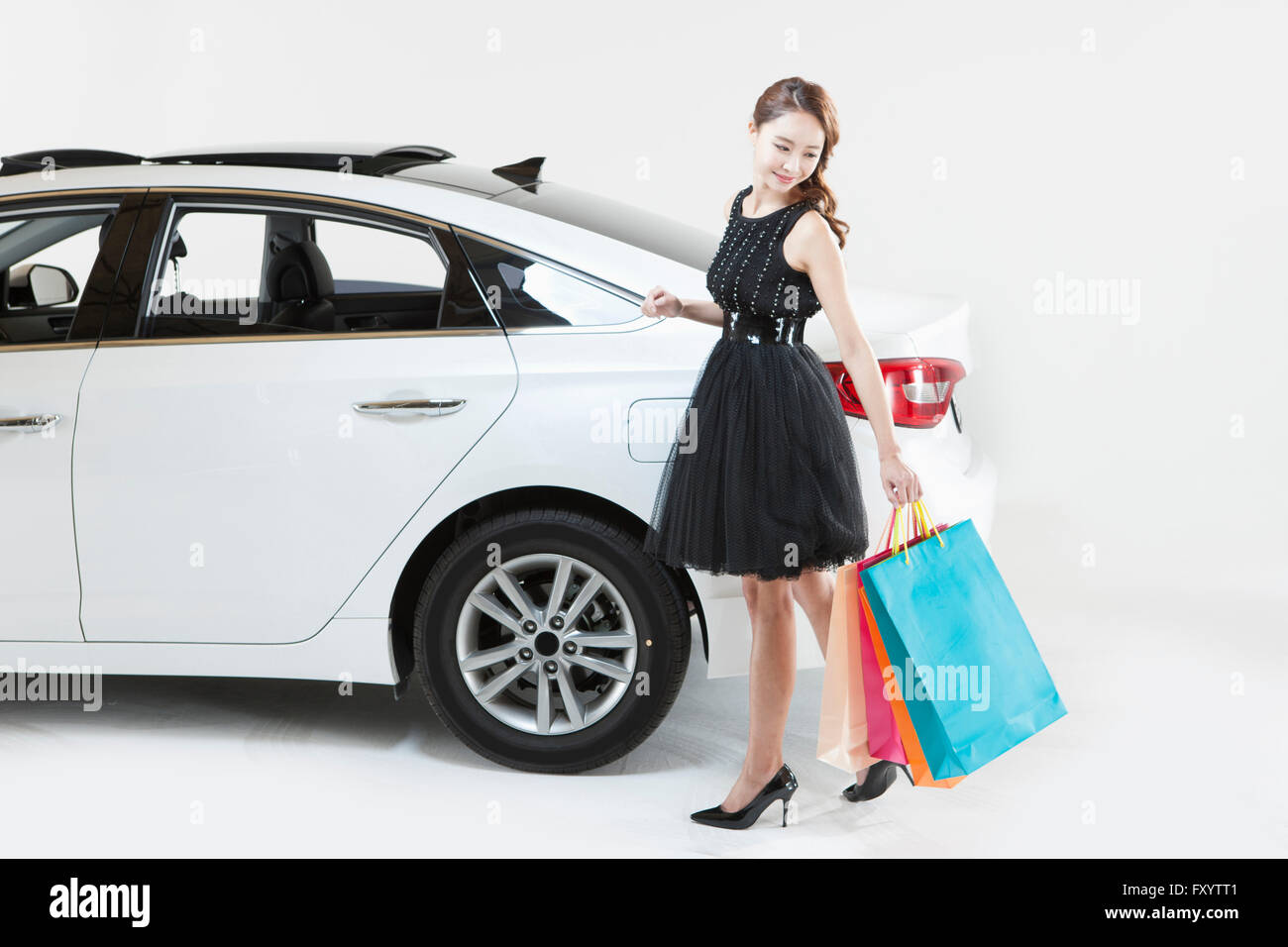 Young smiling woman in dress walking holding shopping bags looking back with a car Stock Photo