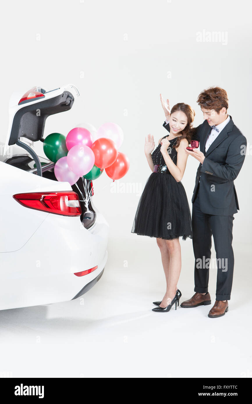 Young man proposing to young woman behind a car Stock Photo