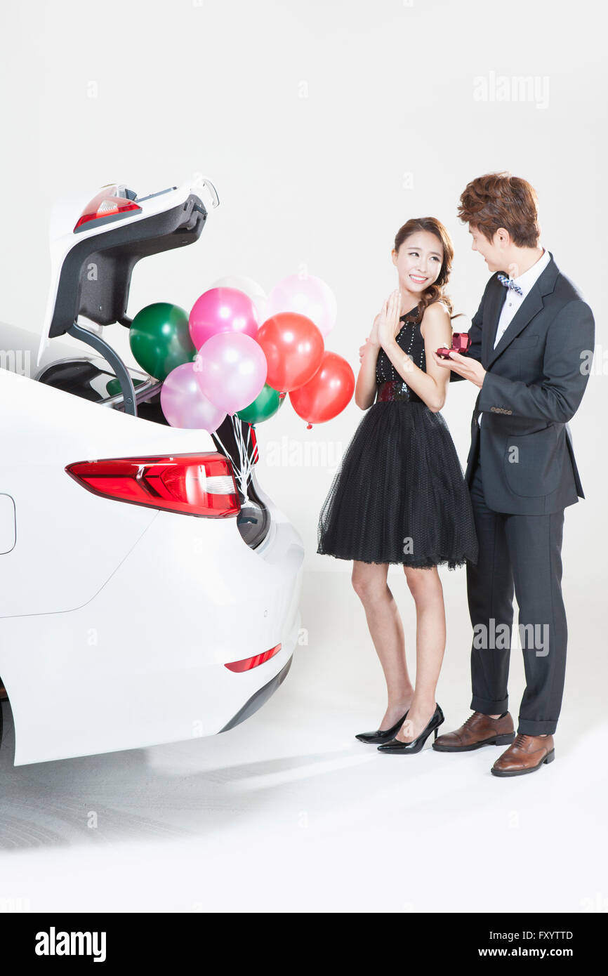 Young man proposing to young woman with a present behind a car Stock Photo