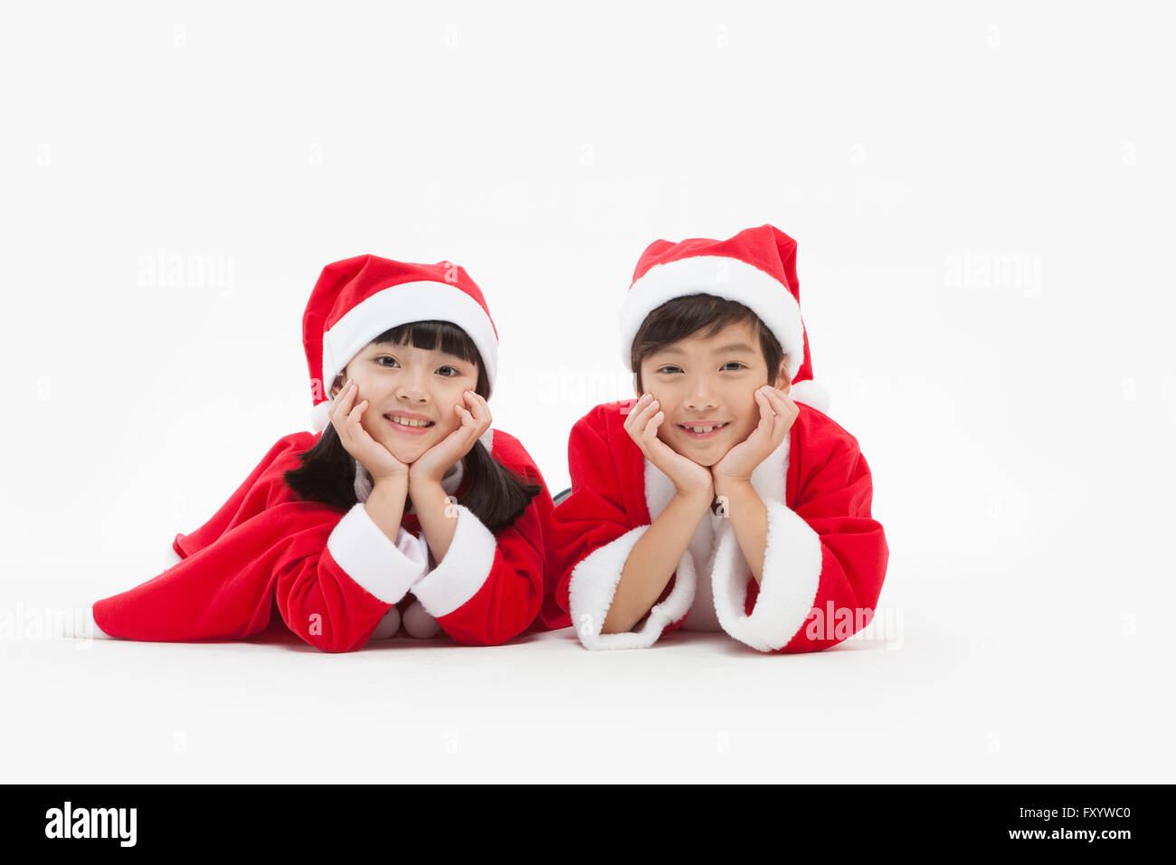 Portrait of smiling boy and girl in santa's clothes placing their chins in their hands staring at front Stock Photo