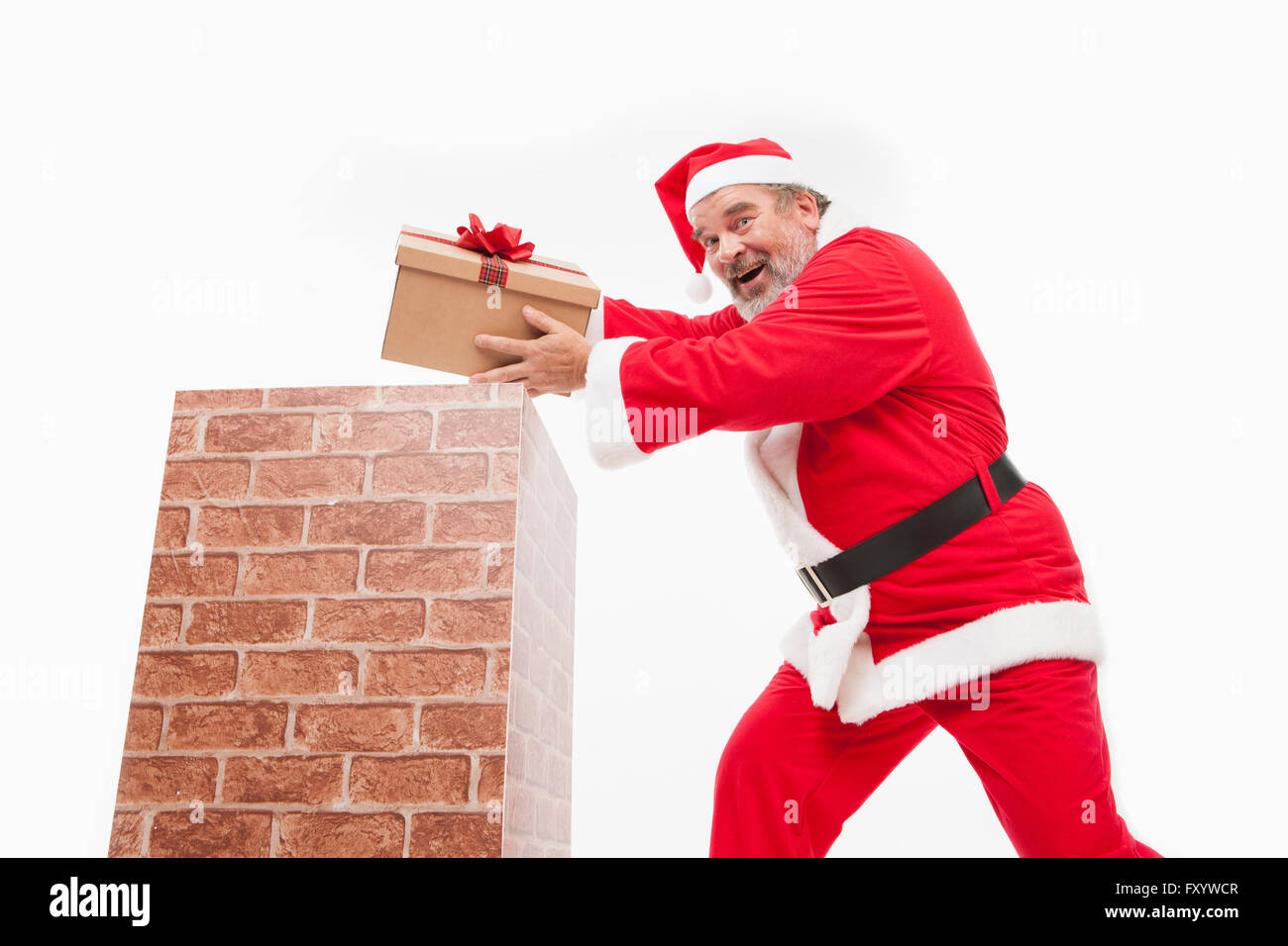 Side view of smiling Santa putting a present box into a chimney staring at front Stock Photo